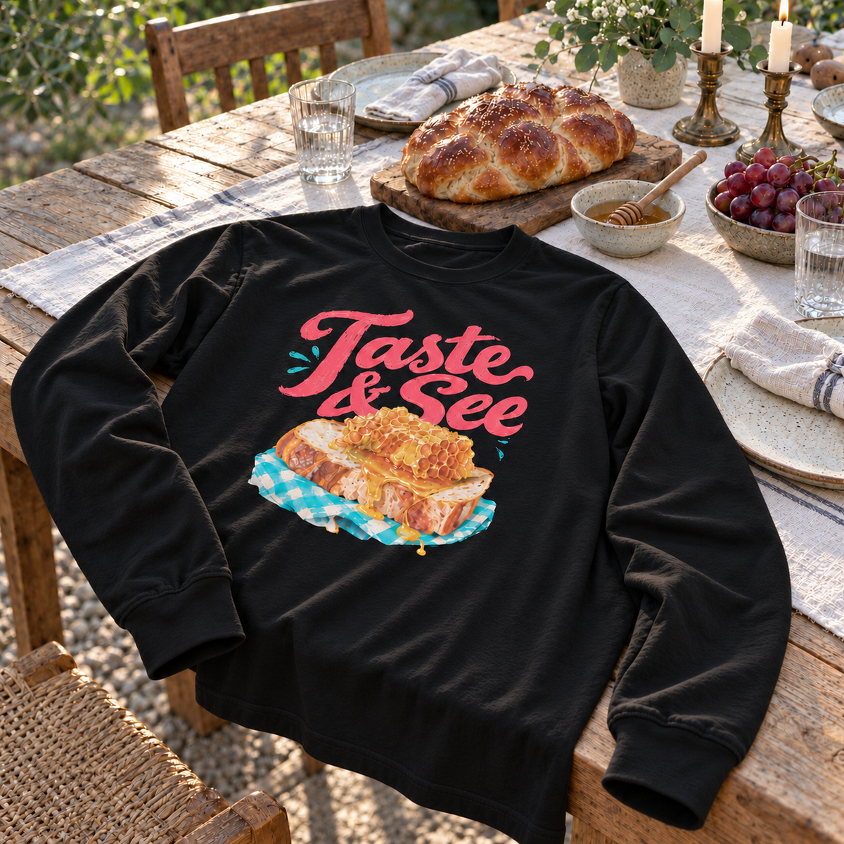 Black Taste and See Psalm 34:8 long-sleeve tee arranged on a Shabbat table with challah, honey, grapes, and candles